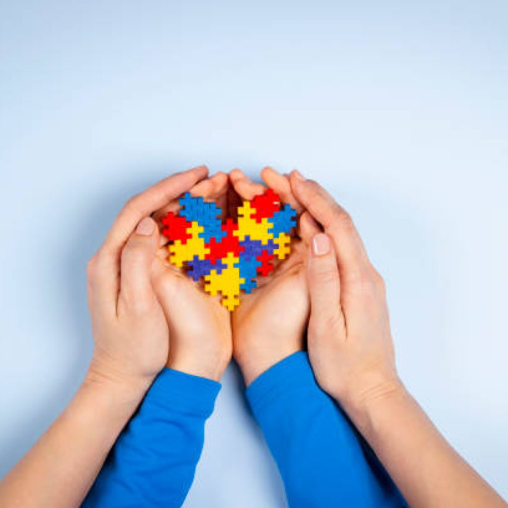 World autism awareness day concept. Adult and child hands holding puzzle heart on light blue background. Top view.